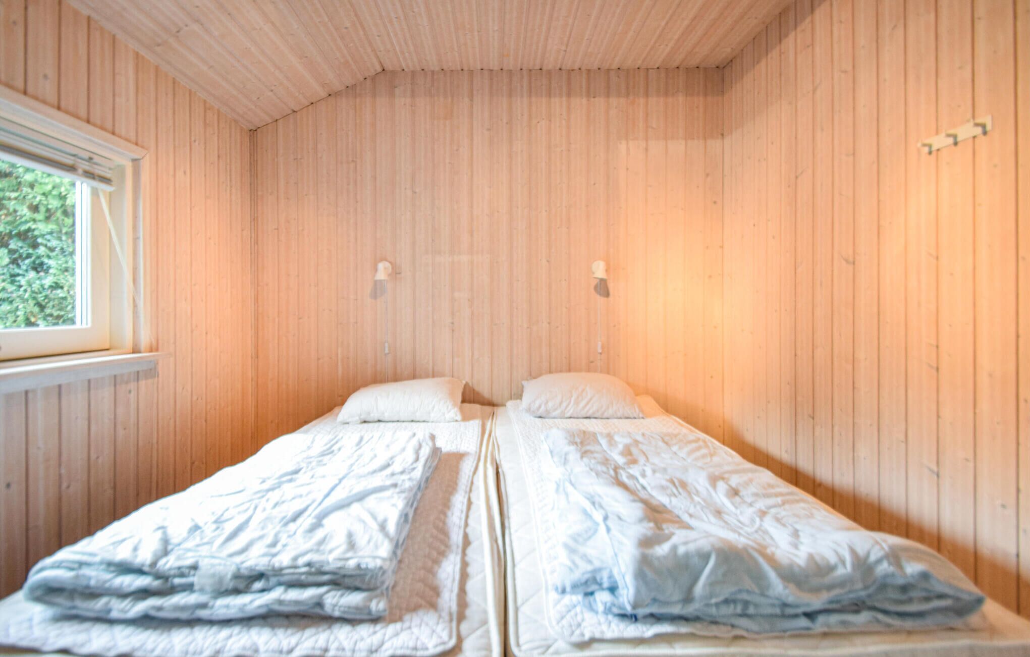 Une chambre avec deux lits simples, des murs en bois, une fenêtre et deux lampes fixées au mur.