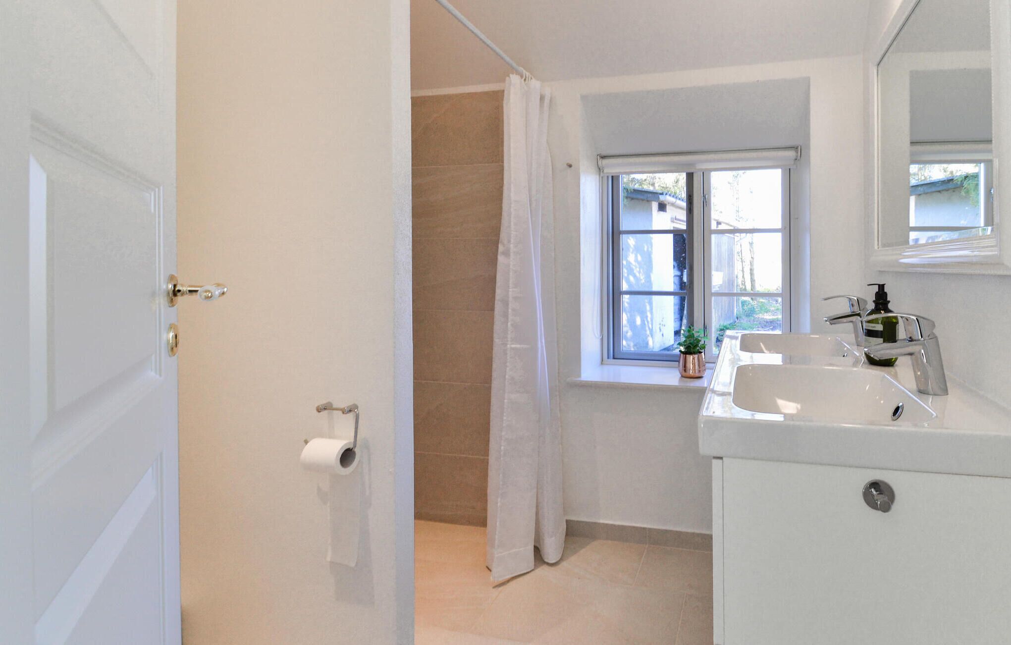 A bathroom with a toilet, a sink, a window with a view, and a shower curtain.