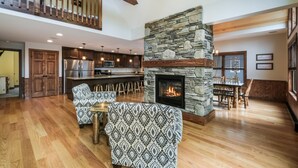 A spacious living room with a stone fireplace, wooden flooring, and a high ceiling with exposed beams. - Rainier by PMR, 8BR, Elevator, Outdoor Fireplace, Double Kitchen, Sleeps 26 (Lake Harmony)