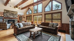 A spacious living room with large windows, a stone fireplace, and a ceiling fan. - Rainier by PMR, 8BR, Elevator, Outdoor Fireplace, Double Kitchen, Sleeps 26 (Lake Harmony)