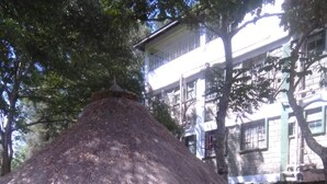 A thatched-roof structure with a circular base, surrounded by trees and a building in the background. - Green Court Hotel (Bondo)