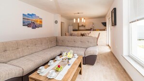 A modern living room with a sectional sofa, a dining table set with plates and cups, and a kitchen in the background. - Beautiful home in Pula (Pula)