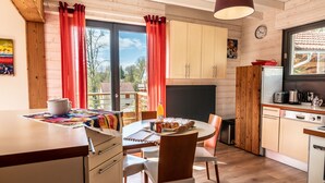 Una cocina acogedora con armarios de madera, una mesa de comedor con sillas, un refrigerador y una ventana con cortinas.
