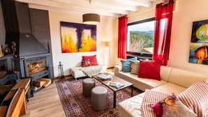 Una sala de estar acogedora con chimenea, un sofá, una mesita de centro y un amplio ventanal con vistas al exterior.