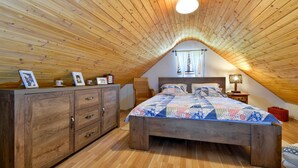 Une chambre à coucher avec un plafond en bois, un lit recouvert d’une courtepointe, une table de chevet, une chaise et une armoire en bois.