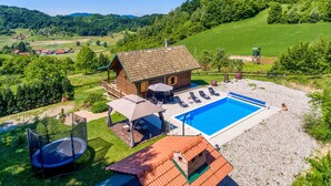 Une cabane en bois avec une piscine, entourée d’un jardin clôturé et d’un trampoline.
