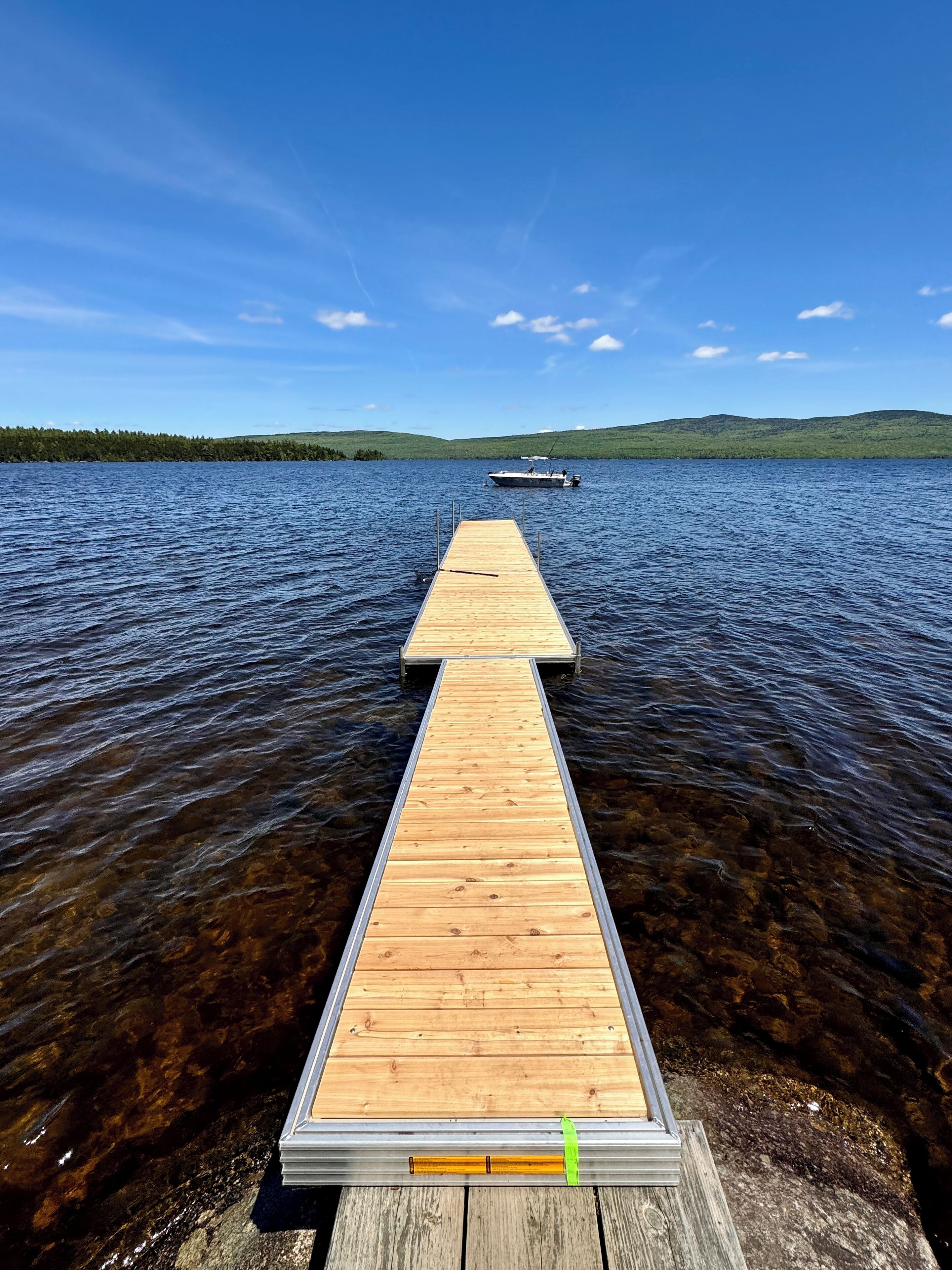 A wooden dock extending into a lake with a boat in the distance and hills in the background.