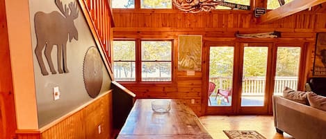 A wooden interior with a dining table, benches, a mounted moose head, and a chandelier.