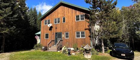 A two-story wooden building with a green roof, a satellite dish, and a small garden with a statue and a gazebo.