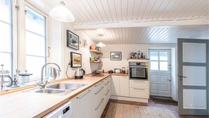 Eine Küche mit weißen Schränken, einem Geschirrspüler, einer Spüle, einem Herd und einem Kühlschrank. Es gibt Regale mit verschiedenen Küchenutensilien und ein Fenster über der Spüle.
