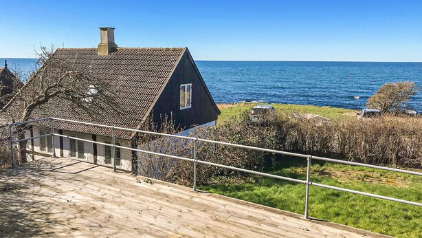 Ein Küstenhaus mit steilem Dach, einem sichtbaren Schornstein und einer Holzterrasse mit Blick auf das Meer.