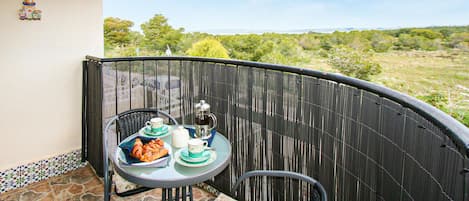 A small balcony with a table set for two, featuring a teapot, cups, and pastries.