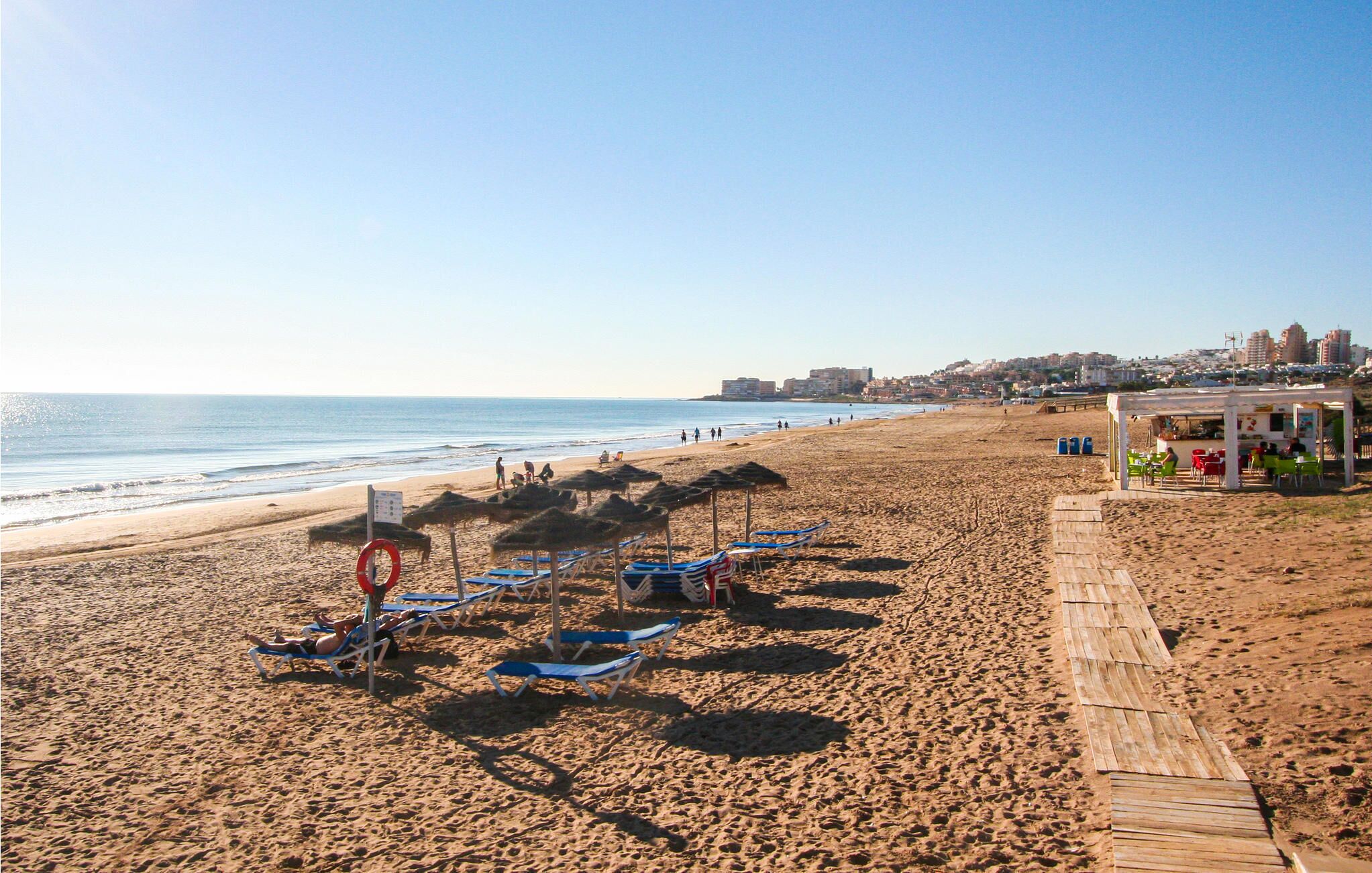 A beach with sun loungers, a lifebuoy, and a wooden walkway.