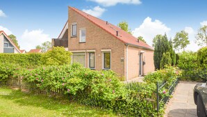 A two-story brick house with a red-tiled roof, a front door, and a small garden with pink flowers. - Stunning home in Breskens with kitchen (Breskens)