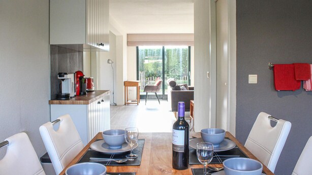 A modern dining area with a wooden table set for four, a wine bottle, and a view of a balcony with a chair. - Stunning home in Breskens with kitchen (Breskens)