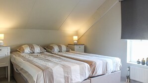 A bedroom with a sloped ceiling, two bedside tables with lamps, a bed with striped bedding, and a window with a view of bottles on the sill. - Stunning home in Breskens with kitchen (Breskens)