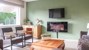 A living room with a green wall, a flat-screen TV, a wooden cabinet, and two armchairs. - Stunning home in Breskens with kitchen (Breskens)