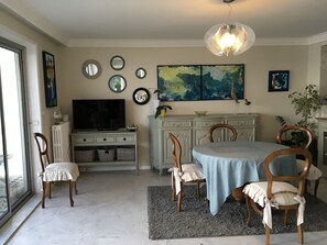 Un coin repas comprenant une table ronde, quatre chaises, un téléviseur, des miroirs décoratifs et des œuvres d’art accrochées aux murs.