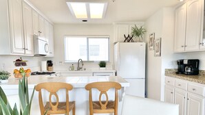 Una cocina moderna con armarios blancos, una isla central con sillas, un refrigerador y una cafetera.