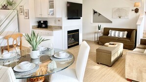 Una sala moderna con una mesa de comedor de cristal, sofás blancos y una chimenea.