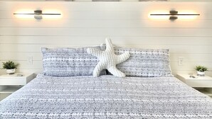 Una cama con una almohada en forma de estrella de mar, una pared con tres cuadros y mesitas de noche con plantas.