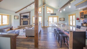 A spacious living area with a fireplace, wooden beams, and a kitchen with bar stools. - Crystal clear Mountain View’s with a farmhouse chic vibe. (Sturgis)