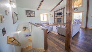 A spacious living area with a fireplace, a staircase with wooden railings, and a large window providing natural light. - Crystal clear Mountain View’s with a farmhouse chic vibe. (Sturgis)