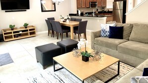 A modern living room with a sofa, coffee table, and dining area. - Spacious3 bdr w/ private jacuzzi private jacuzzi! (Kissimmee)