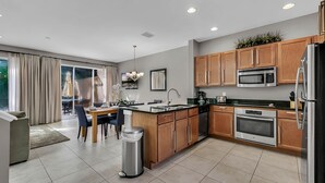 A modern kitchen with wooden cabinets, stainless steel appliances, and a dining area with a table and chairs. - Spacious3 bdr w/ private jacuzzi private jacuzzi! (Kissimmee)