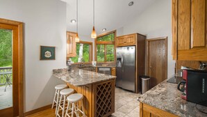 Una cocina con gabinetes de madera, un refrigerador de acero inoxidable, un enfriador de vinos empotrado y una isla grande con taburetes.