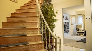 Una escalera de madera con detalles en pared de piedra, una planta en maceta y una silla con cojín.