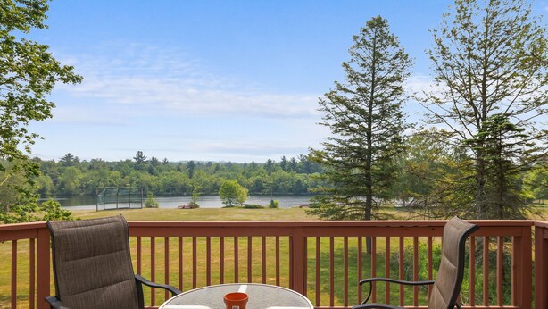 Una terraza con dos sillas y una mesa, con vista a un lago y un bosque.