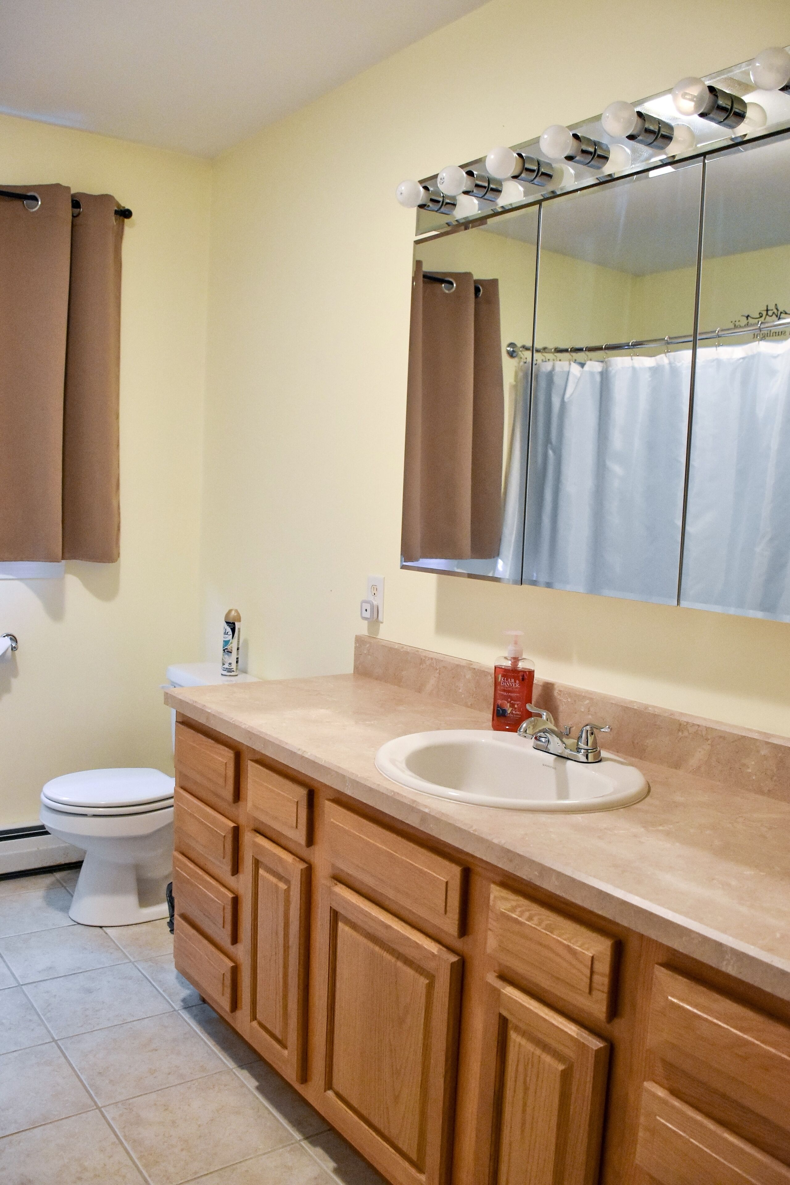 A bathroom with a beige countertop, wooden cabinets, a white sink, a mirror with lights, a toilet, and brown towels.
