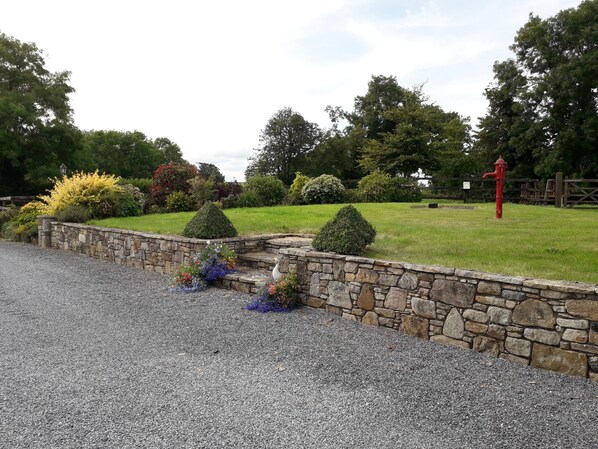 A landscaped garden with a stone wall, trimmed bushes, and a red fire hydrant.