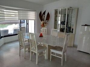 A dining area with a white table and chairs, a glass cabinet with dishes, and a refrigerator.