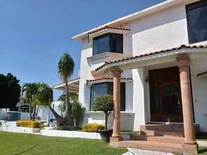 A two-story house with a white exterior, red-tiled roof, and a front porch with columns.