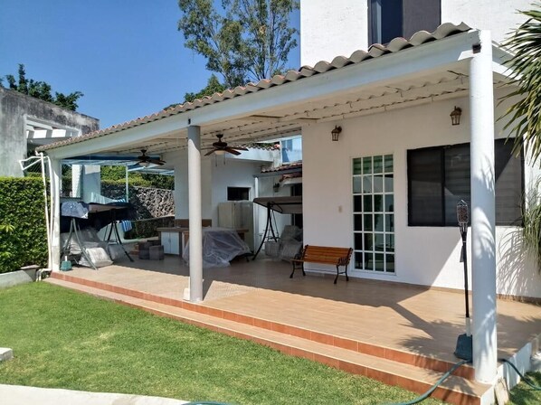 A covered patio area with a ceiling fan, a barbecue grill, and a bench.