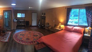 A cozy room with a bed, a sofa, and a small table. There is a window with curtains, a door, and a mirror on the wall.
