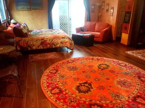 A room with a bed, a sofa, a round rug, and a dining area with chairs and a table.