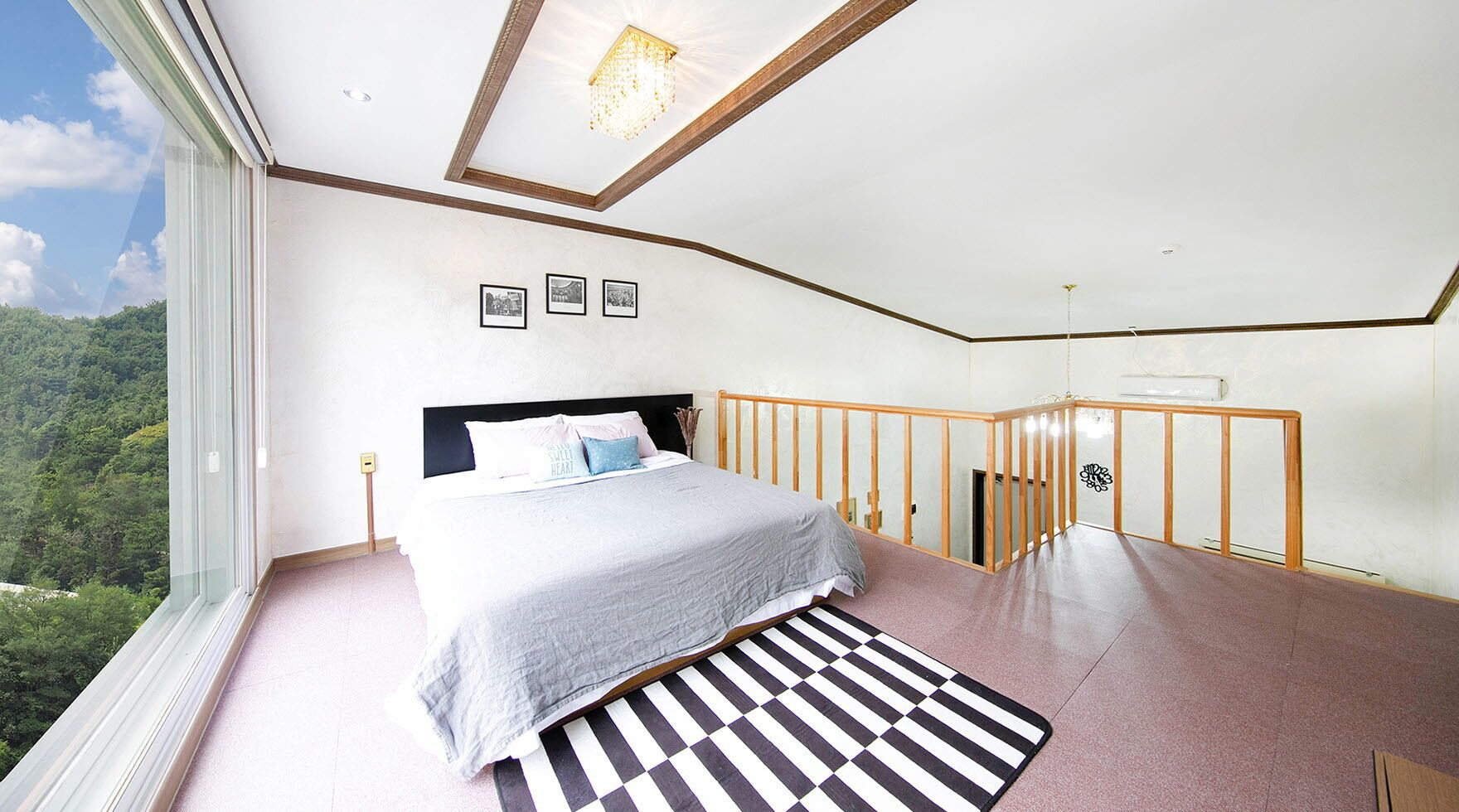 A bedroom with a bed, a view of greenery, and a wooden railing.