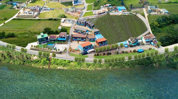 An aerial view of a coastal resort with multiple buildings, a marina, and surrounding agricultural fields. - Kkoristar Pool and Spa Pension (Gapyeong)