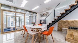 A modern dining area with a round table, orange and white chairs, and a city view through large windows. - Miramonti Pool Villa Pension (Gapyeong)