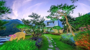 A house with a stone pathway leading to it, surrounded by lush greenery and flowering plants. - Miramonti Pool Villa Pension (Gapyeong)