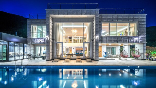 A modern two-story house with a large glass facade, a pool in the foreground, and outdoor seating. - Miramonti Pool Villa Pension (Gapyeong)