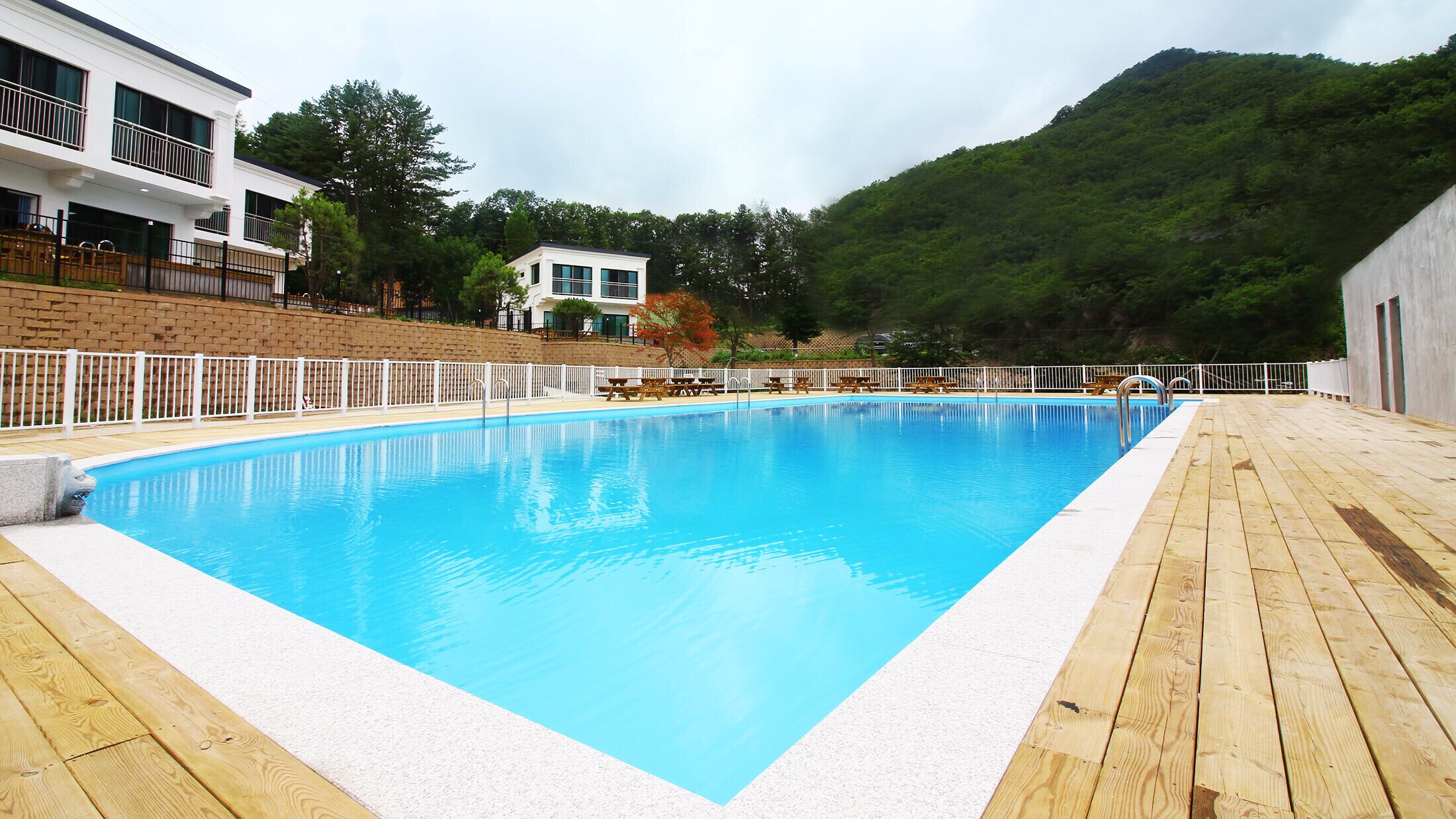Piscina rectangular con muelle de madera que la rodea, con edificios y una colina boscosa de fondo.