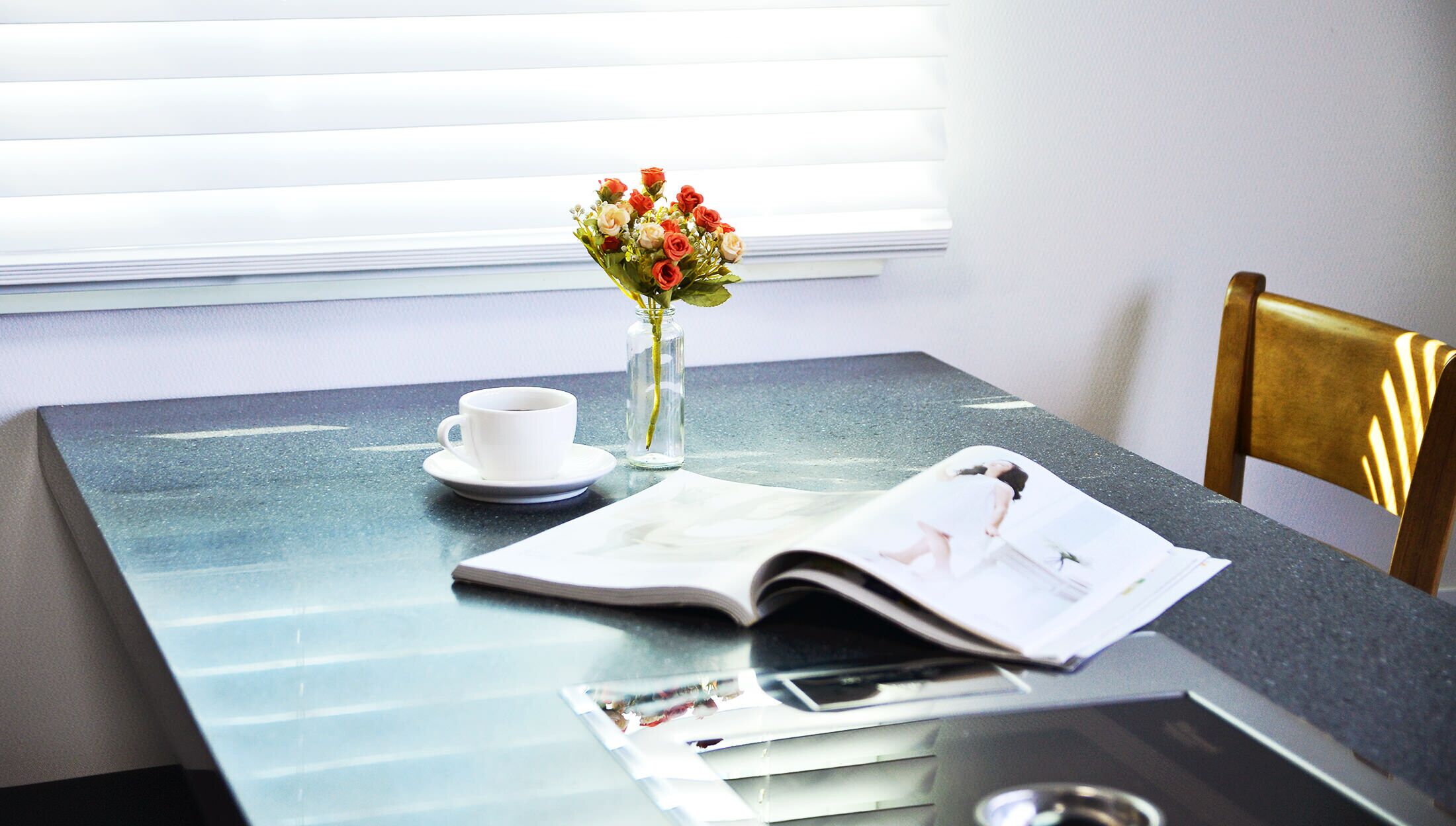 Una mesa con una revista, una taza y un florero con flores.
