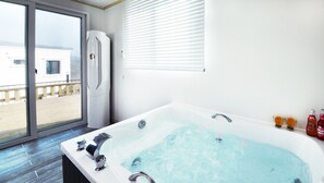 A modern bathroom with a large bathtub, a glass shower enclosure, and a view of the beach through the sliding doors. - Eco Land Pension (Gapyeong)