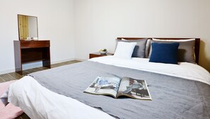 A neatly made bed with a magazine on it, a wooden nightstand with a bowl of fruit, and a mirror on the wall. - Eco Land Pension (Gapyeong)