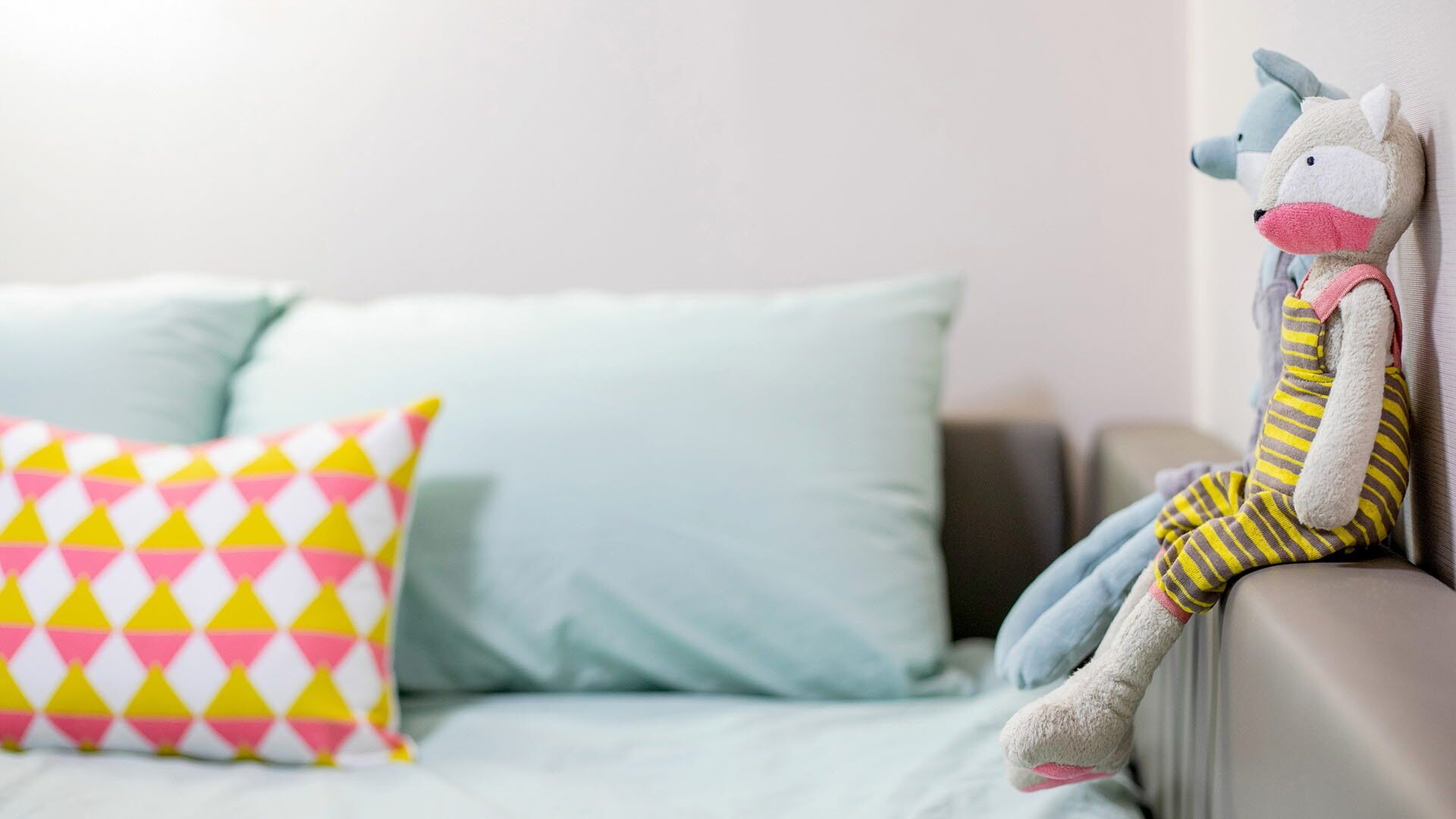 A bed with a light blue mattress and pillows, one with a pink and yellow geometric pattern.