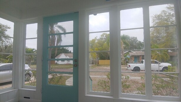 A room with a teal door and large windows overlooking a parking area with a white pickup truck. - Cute Bungalow in Historic Kenwood (St. Petersburg)